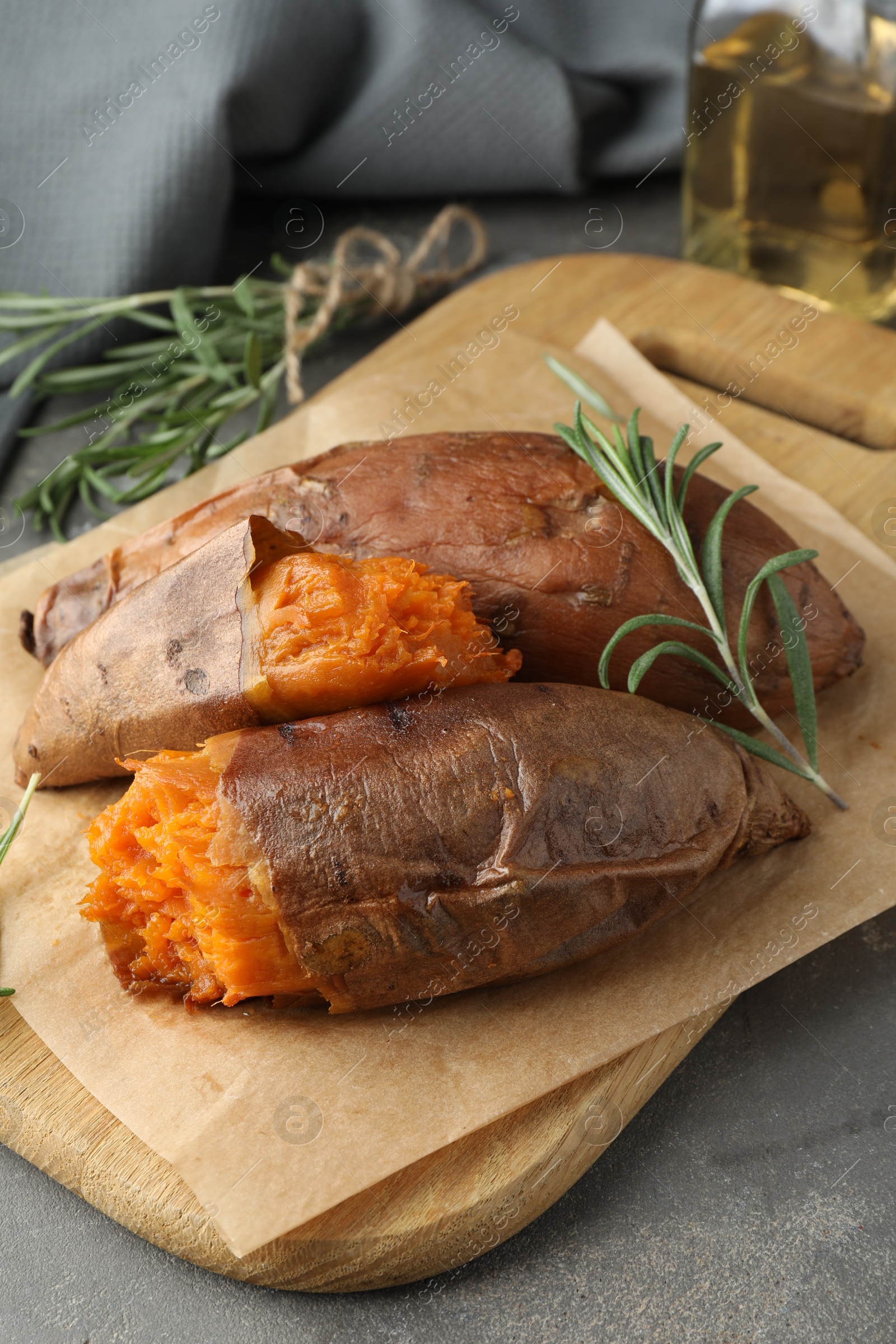 Photo of Tasty cooked sweet potatoes served with rosemary on grey table, closeup