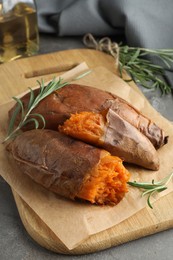 Photo of Tasty cooked sweet potatoes served with rosemary on grey table, closeup