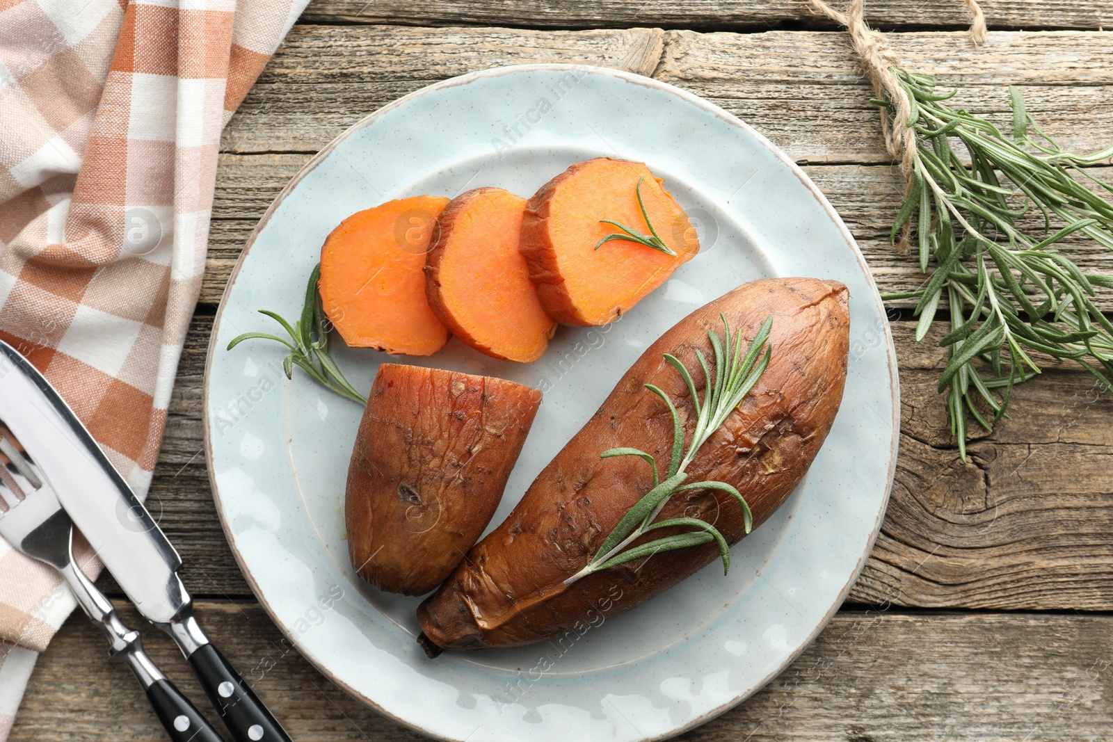 Photo of Tasty cooked sweet potatoes served with rosemary and cutlery on wooden table, flat lay