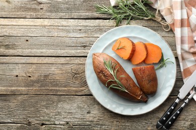 Photo of Tasty cooked sweet potatoes served with rosemary and cutlery on wooden table, flat lay. Space for text