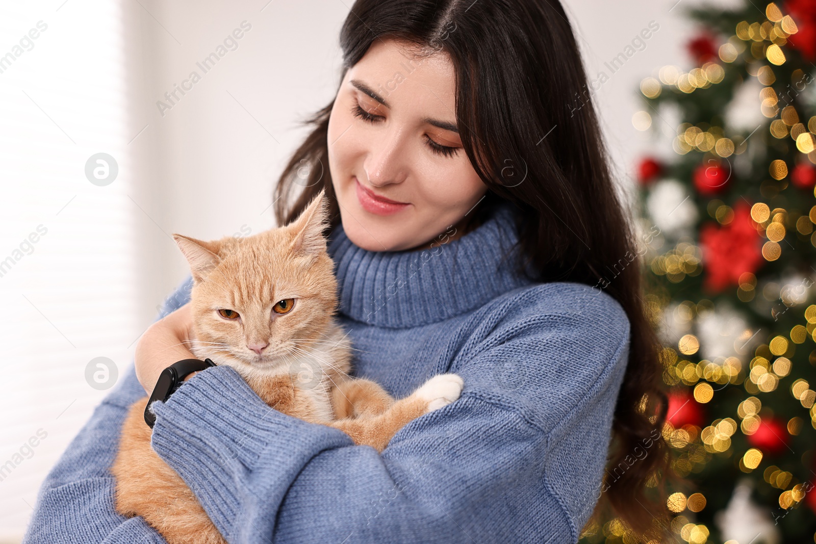 Photo of Woman with cute ginger cat in room decorated for Christmas