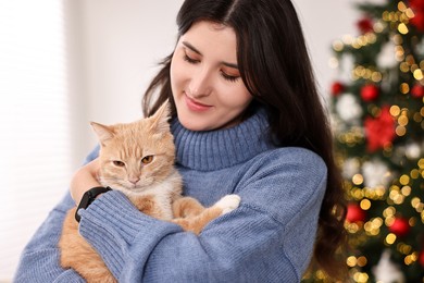 Photo of Woman with cute ginger cat in room decorated for Christmas