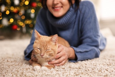 Woman with cute ginger cat against blurred Christmas lights indoors, closeup