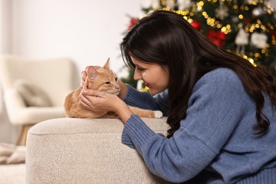 Photo of Woman with cute ginger cat in room decorated for Christmas