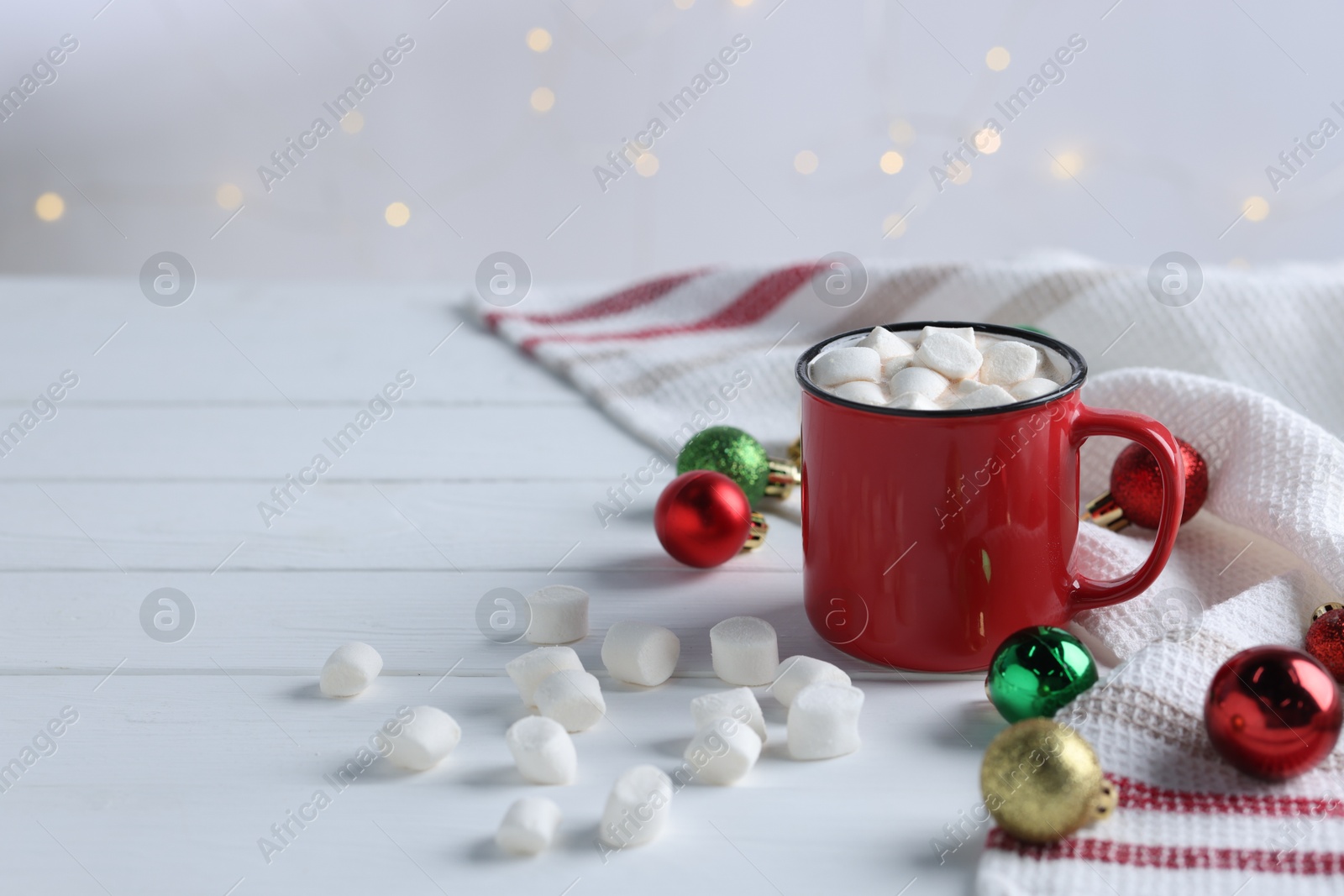 Photo of Yummy cocoa with marshmallows in red cup and Christmas balls on white wooden table, space for text