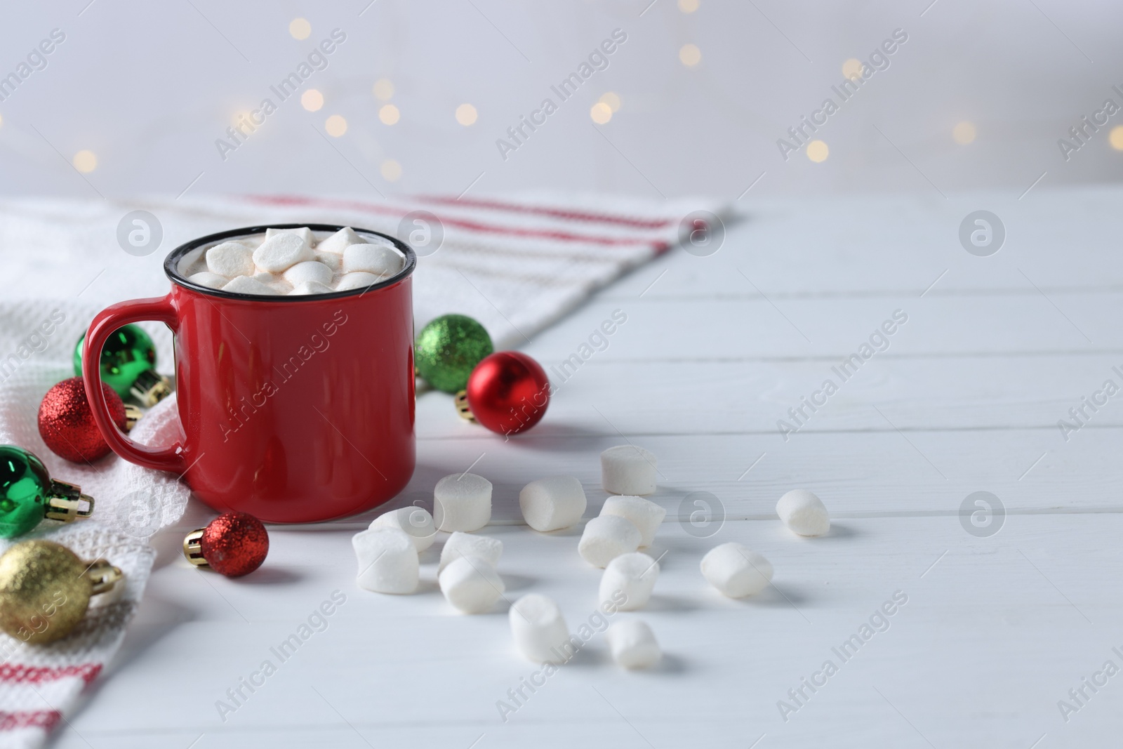 Photo of Yummy cocoa with marshmallows in red cup and Christmas balls on white wooden table, space for text