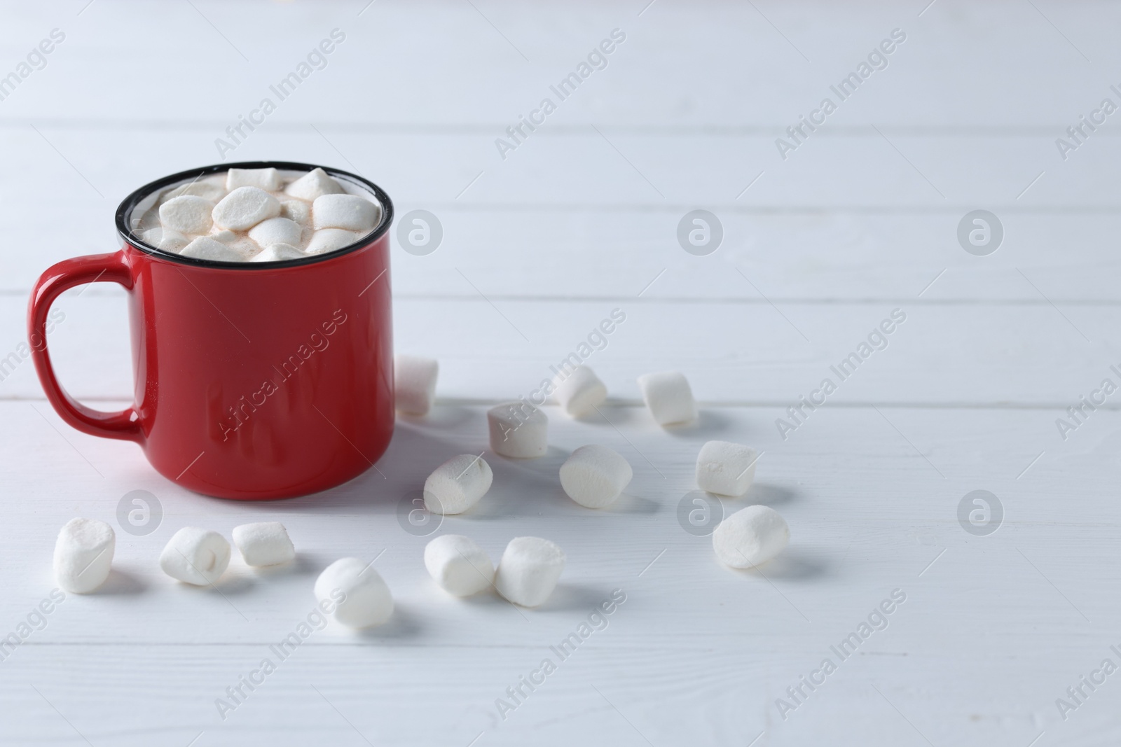 Photo of Yummy cocoa with marshmallows in red cup on white wooden table, space for text