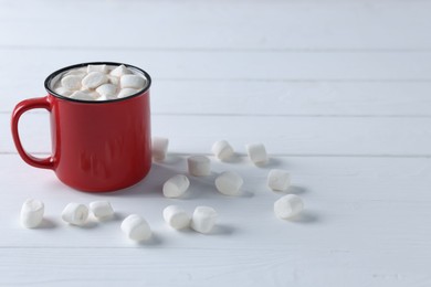 Photo of Yummy cocoa with marshmallows in red cup on white wooden table, space for text