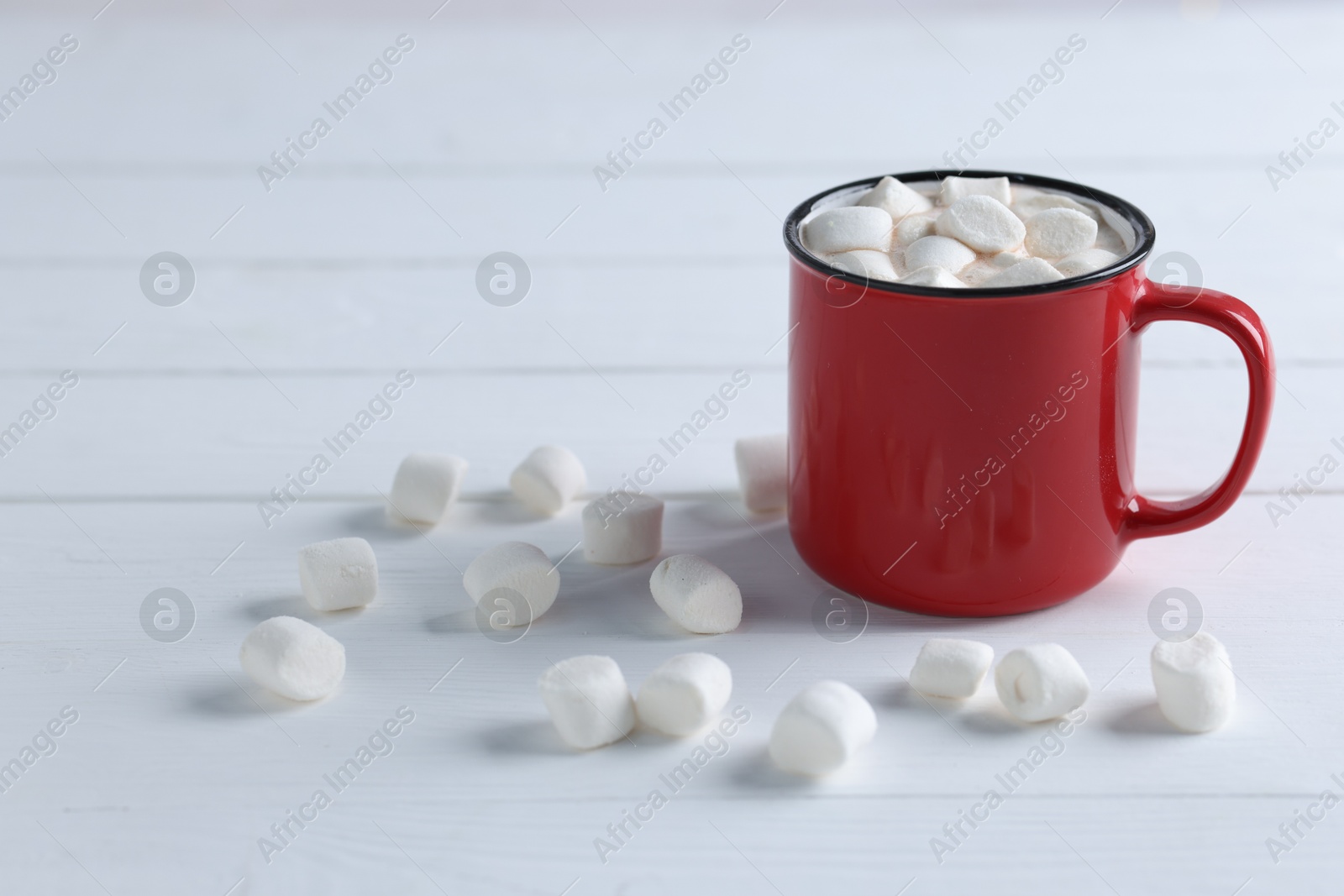 Photo of Yummy cocoa with marshmallows in red cup on white wooden table, space for text