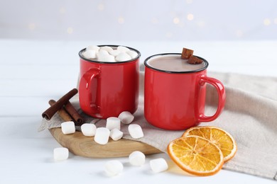 Photo of Yummy cocoa with marshmallows, dried orange slices and spices on white wooden table