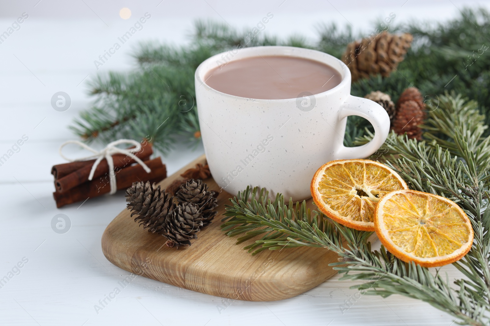 Photo of Yummy cocoa in cup, cinnamon sticks, dried orange slices and fir tree branches on white wooden table