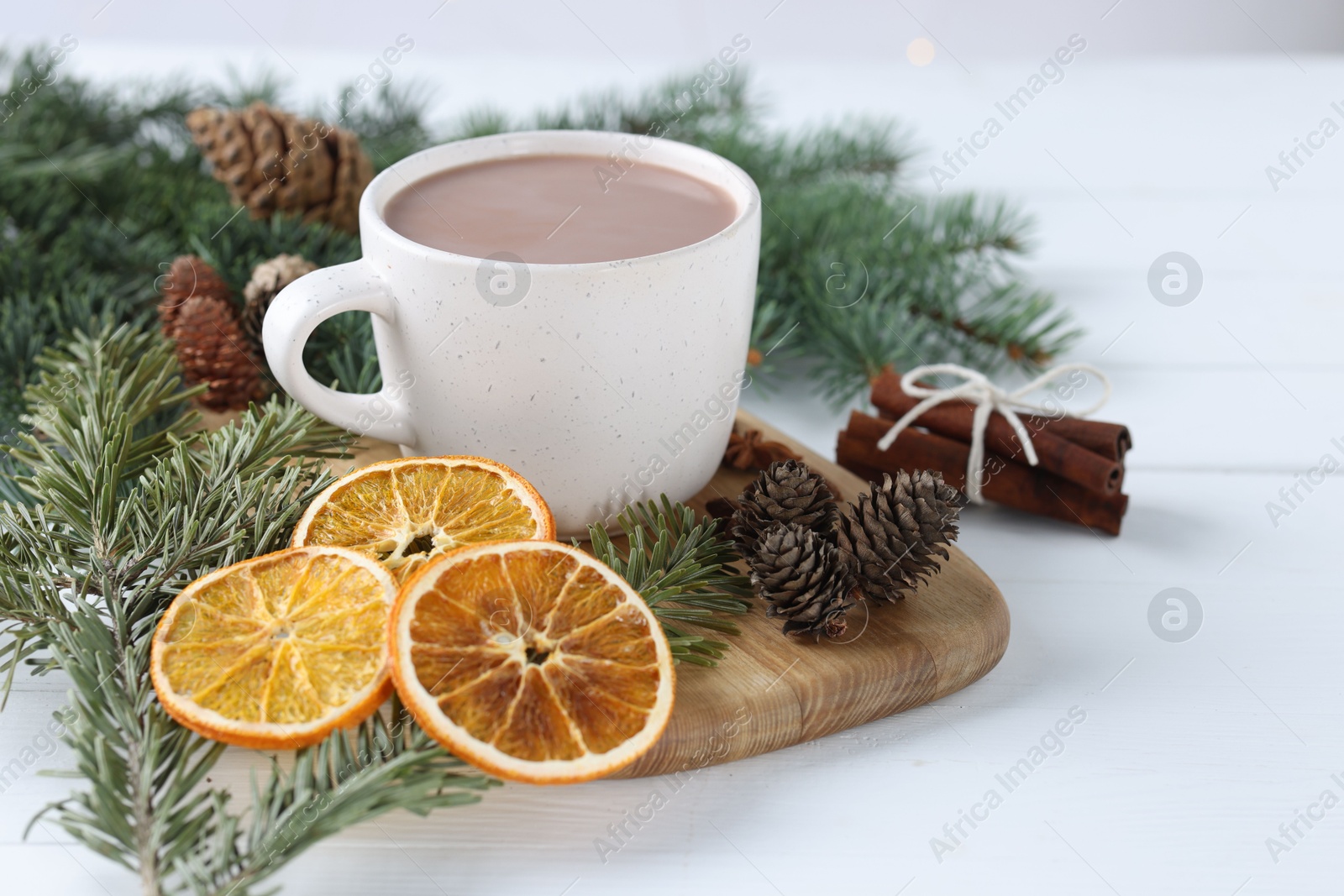 Photo of Yummy cocoa in cup, cinnamon sticks, dried orange slices and fir tree branches on white wooden table