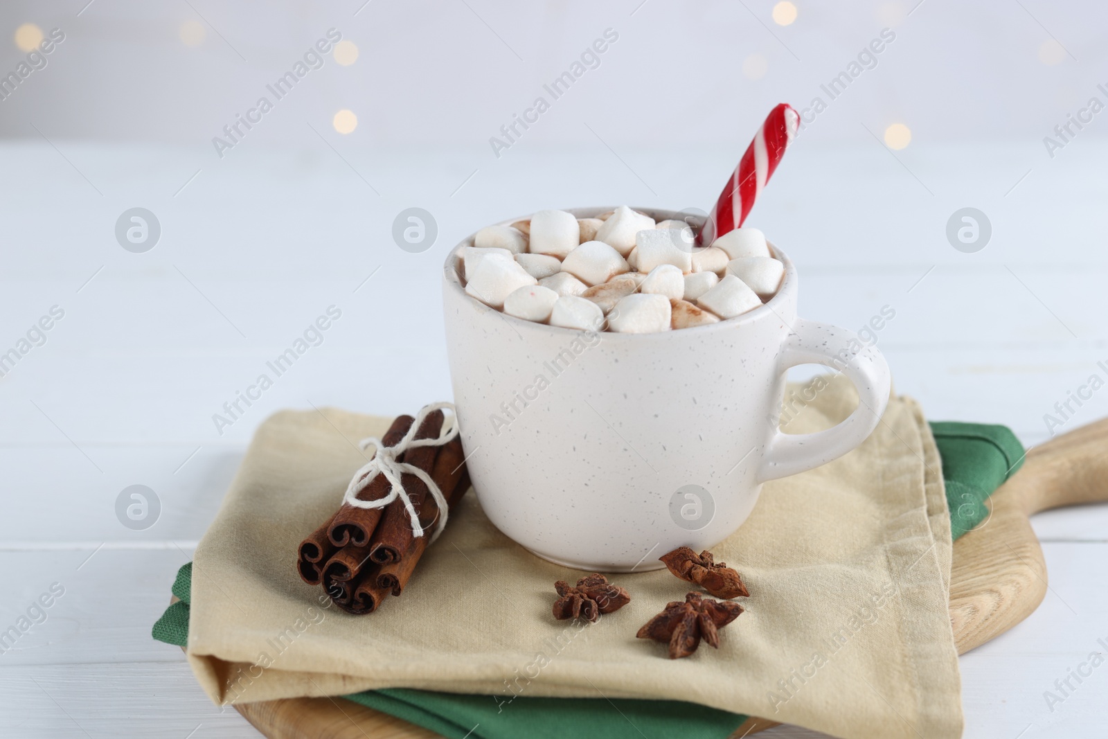 Photo of Yummy cocoa with marshmallows and candy cane in cup and spices on white wooden table