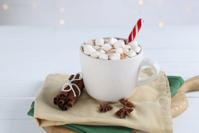 Photo of Yummy cocoa with marshmallows and candy cane in cup and spices on white wooden table