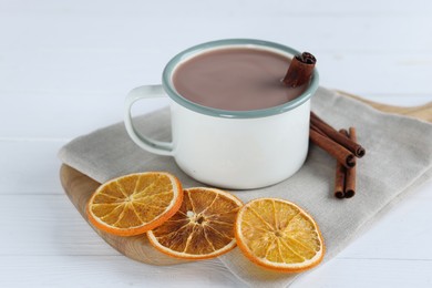 Photo of Yummy cocoa in cup, cinnamon sticks and dried orange slices on white wooden table, closeup