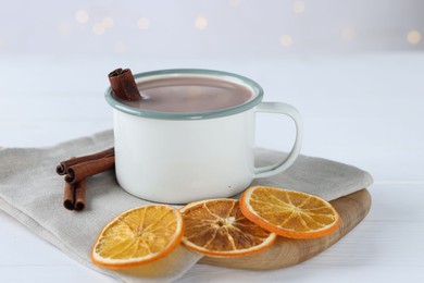 Photo of Yummy cocoa in cup, cinnamon sticks and dried orange slices on white wooden table, closeup