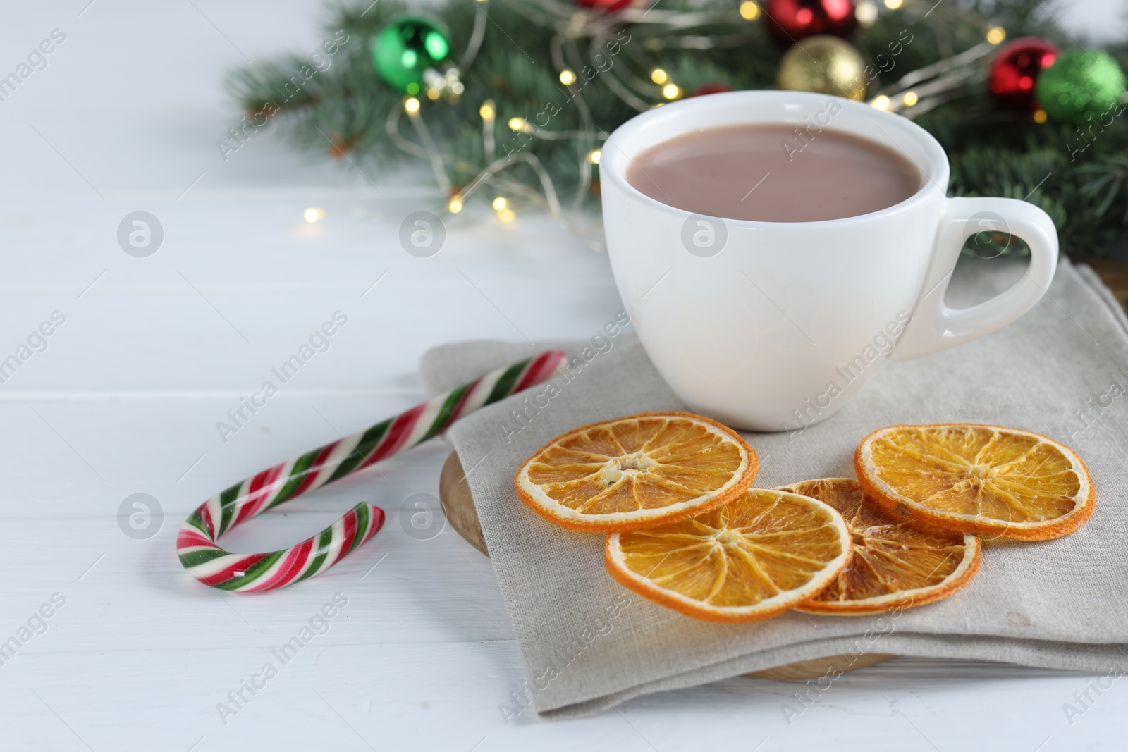 Photo of Yummy cocoa in cup, candy cane, dried orange slices and Christmas wreath on white wooden table. Space for text