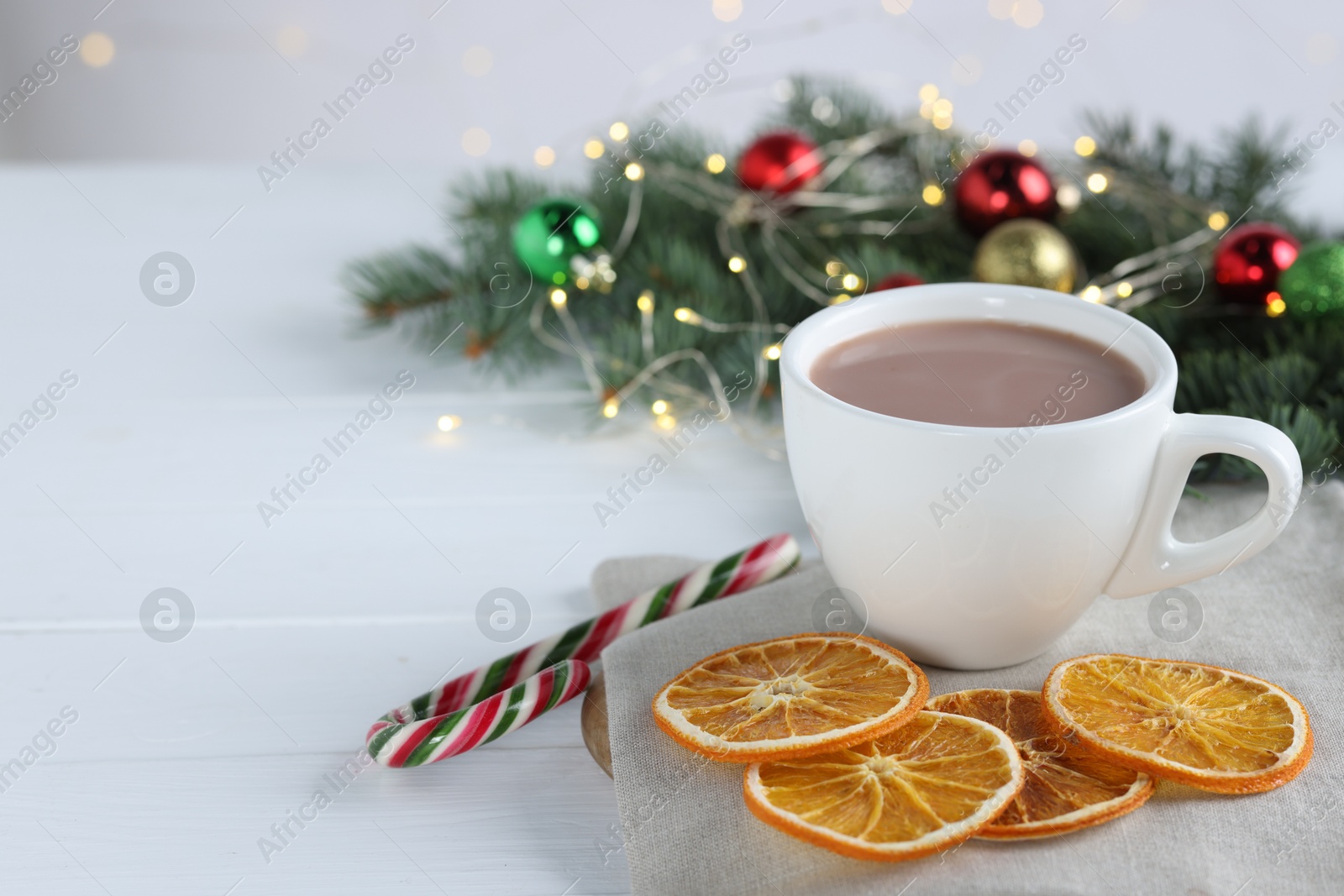 Photo of Yummy cocoa in cup, candy cane, dried orange slices and Christmas wreath on white wooden table. Space for text