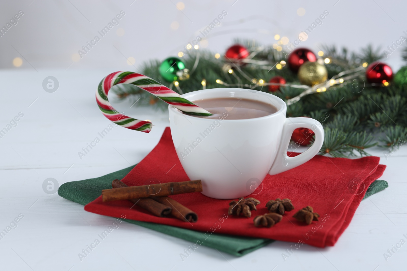 Photo of Yummy cocoa and candy cane in cup, spices and Christmas wreath on white wooden table