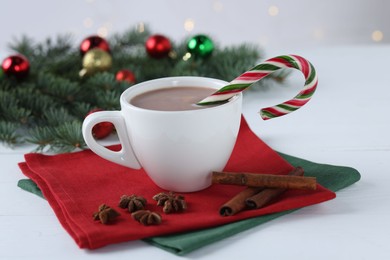 Photo of Yummy cocoa and candy cane in cup, spices and Christmas wreath on white wooden table