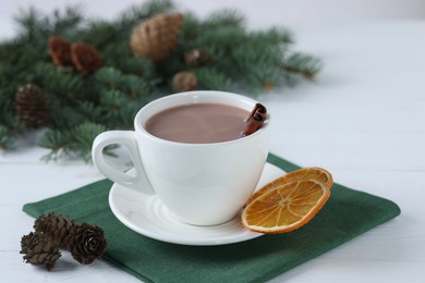 Photo of Yummy cocoa in cup and fir tree branches on white wooden table