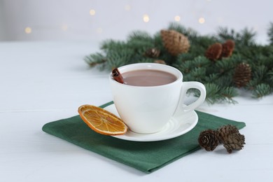 Photo of Yummy cocoa in cup and fir tree branches on white wooden table