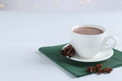 Photo of Yummy cocoa in cup, cinnamon sticks and anise stars on white wooden table. Space for text