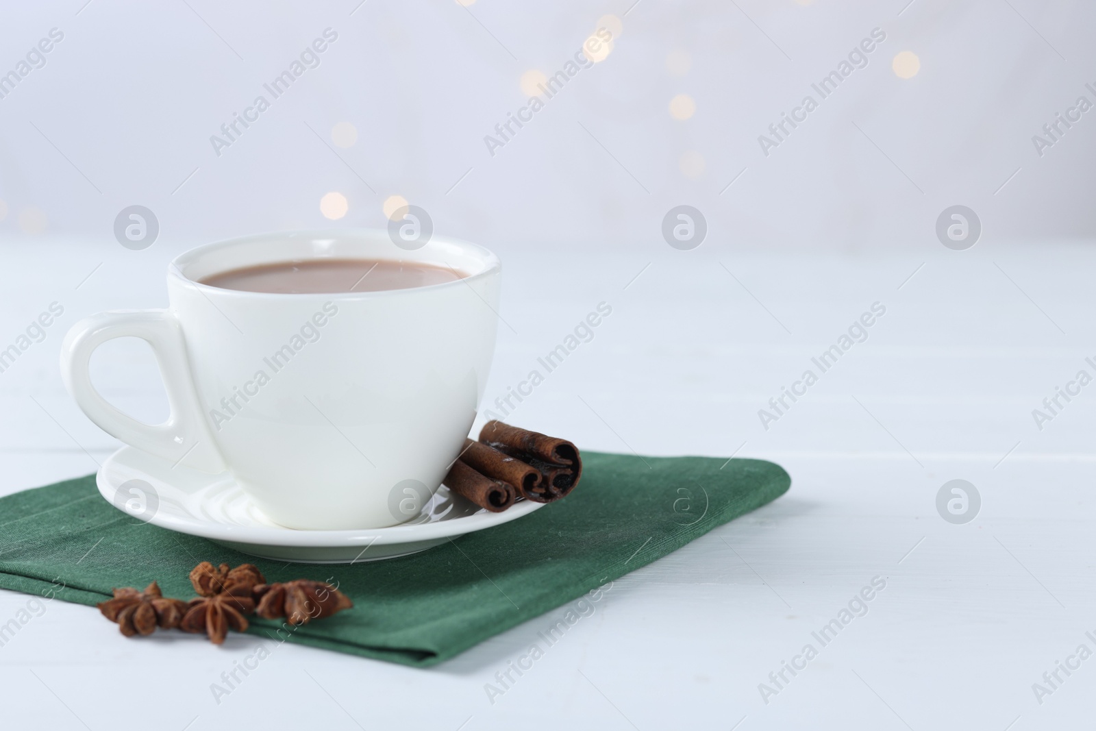 Photo of Yummy cocoa in cup, cinnamon sticks and anise stars on white wooden table. Space for text