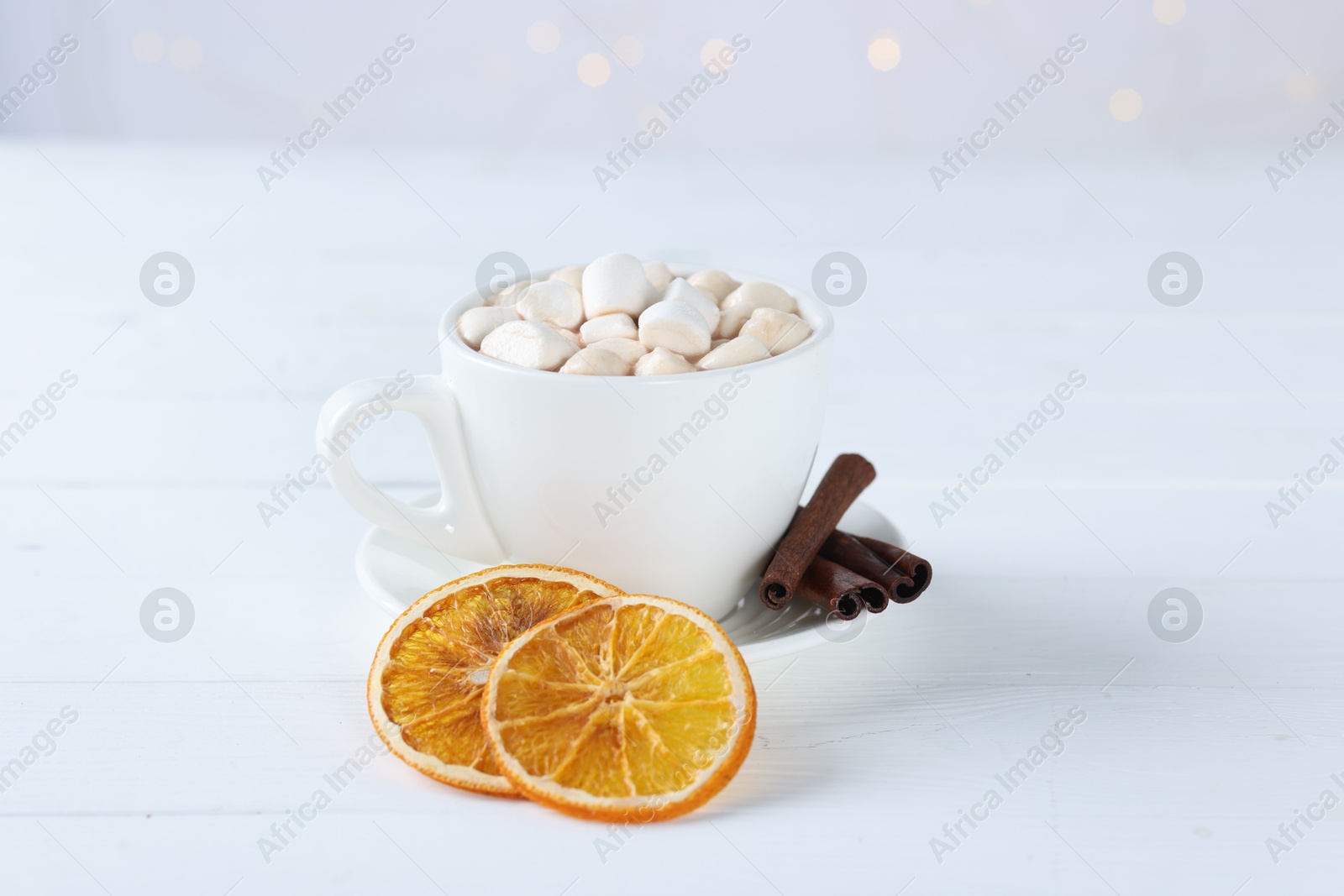 Photo of Yummy cocoa with marshmallows in cup, dried orange slices and spices on white wooden table