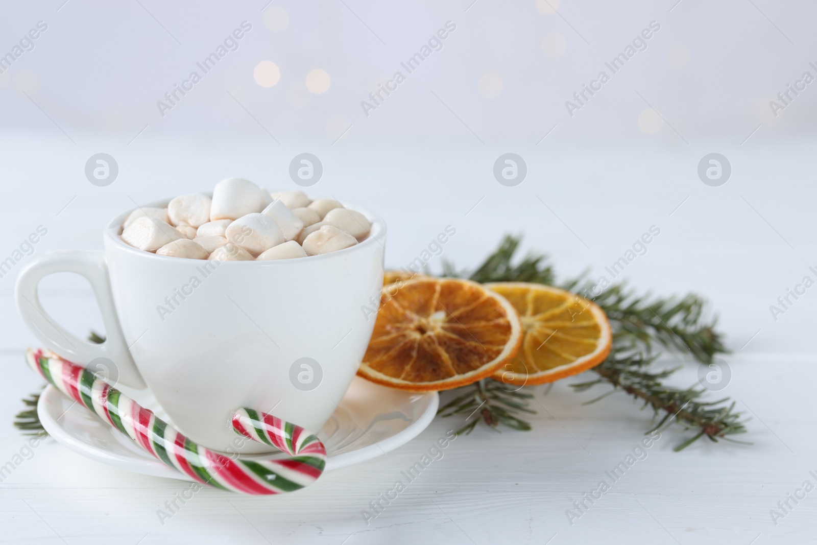 Photo of Yummy cocoa with marshmallows in cup, candy cane, dried orange slices and fir tree branches on white wooden table. Space for text