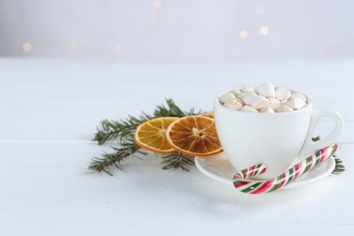 Photo of Yummy cocoa with marshmallows in cup, candy cane, dried orange slices and fir tree branches on white wooden table. Space for text