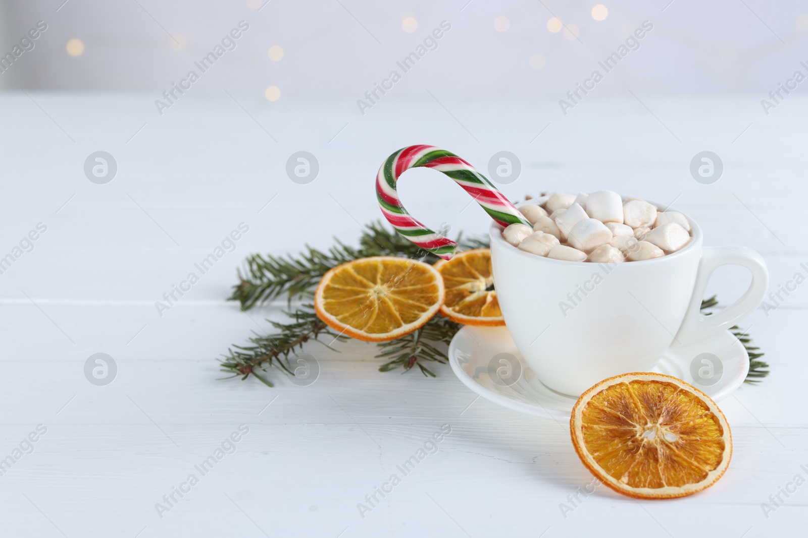 Photo of Yummy cocoa with marshmallows in cup, candy cane, dried orange slices and fir tree branches on white wooden table. Space for text