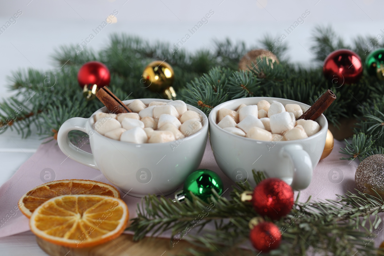 Photo of Yummy cocoa with marshmallows in cups and fir tree branches with Christmas balls on white table