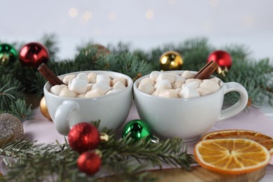 Photo of Yummy cocoa with marshmallows in cups and fir tree branches with Christmas balls on white table