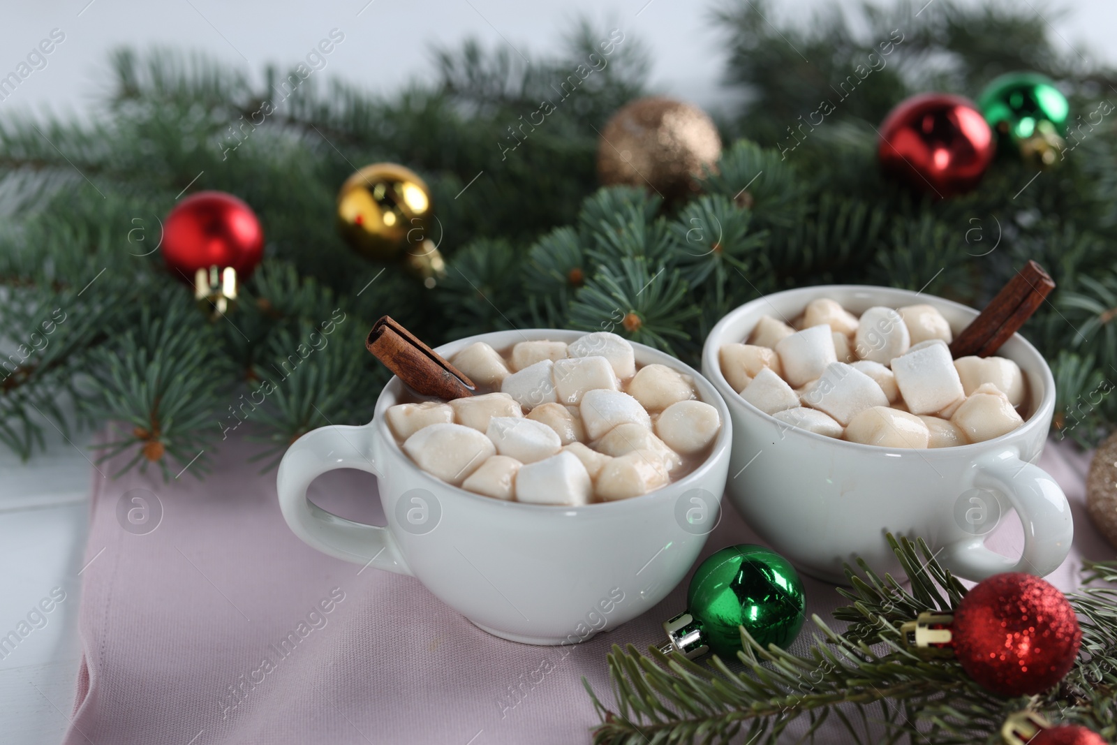 Photo of Yummy cocoa with marshmallows in cups and fir tree branches with Christmas balls on white table