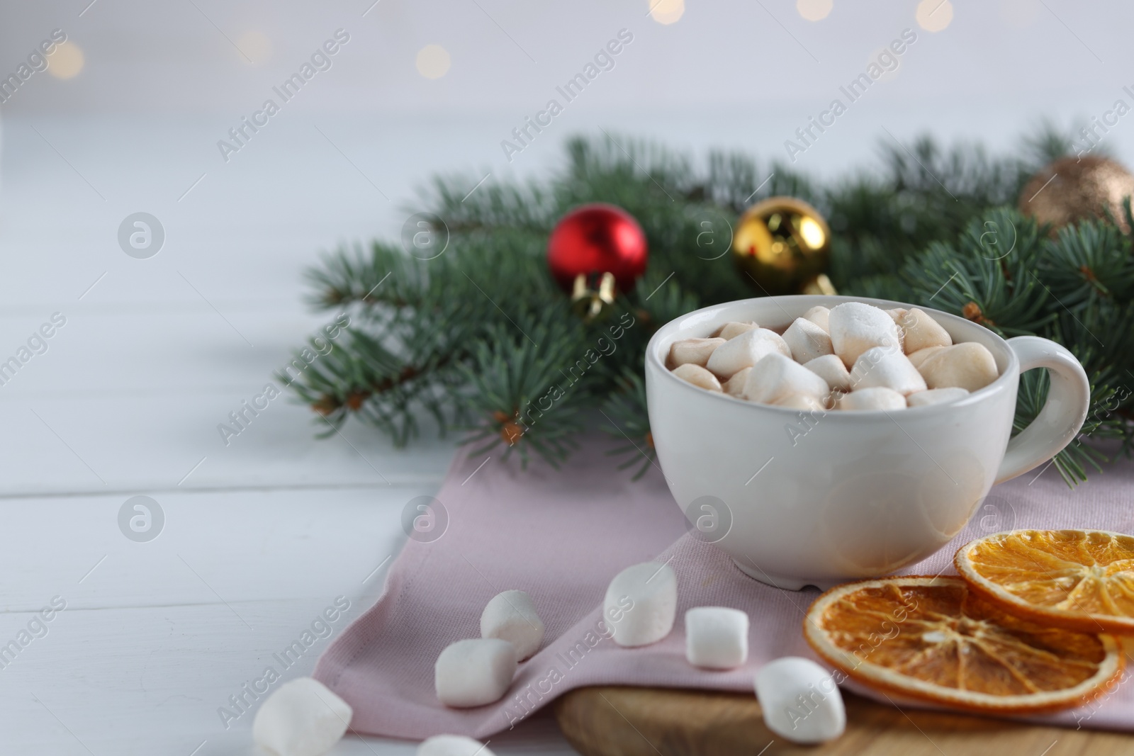 Photo of Yummy cocoa with marshmallows in cup, dried orange slices and Christmas wreath on white wooden table. Space for text