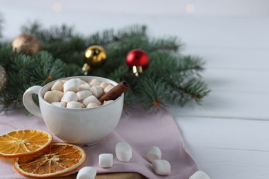 Photo of Yummy cocoa with marshmallows in cup, dried orange slices and Christmas wreath on white wooden table. Space for text