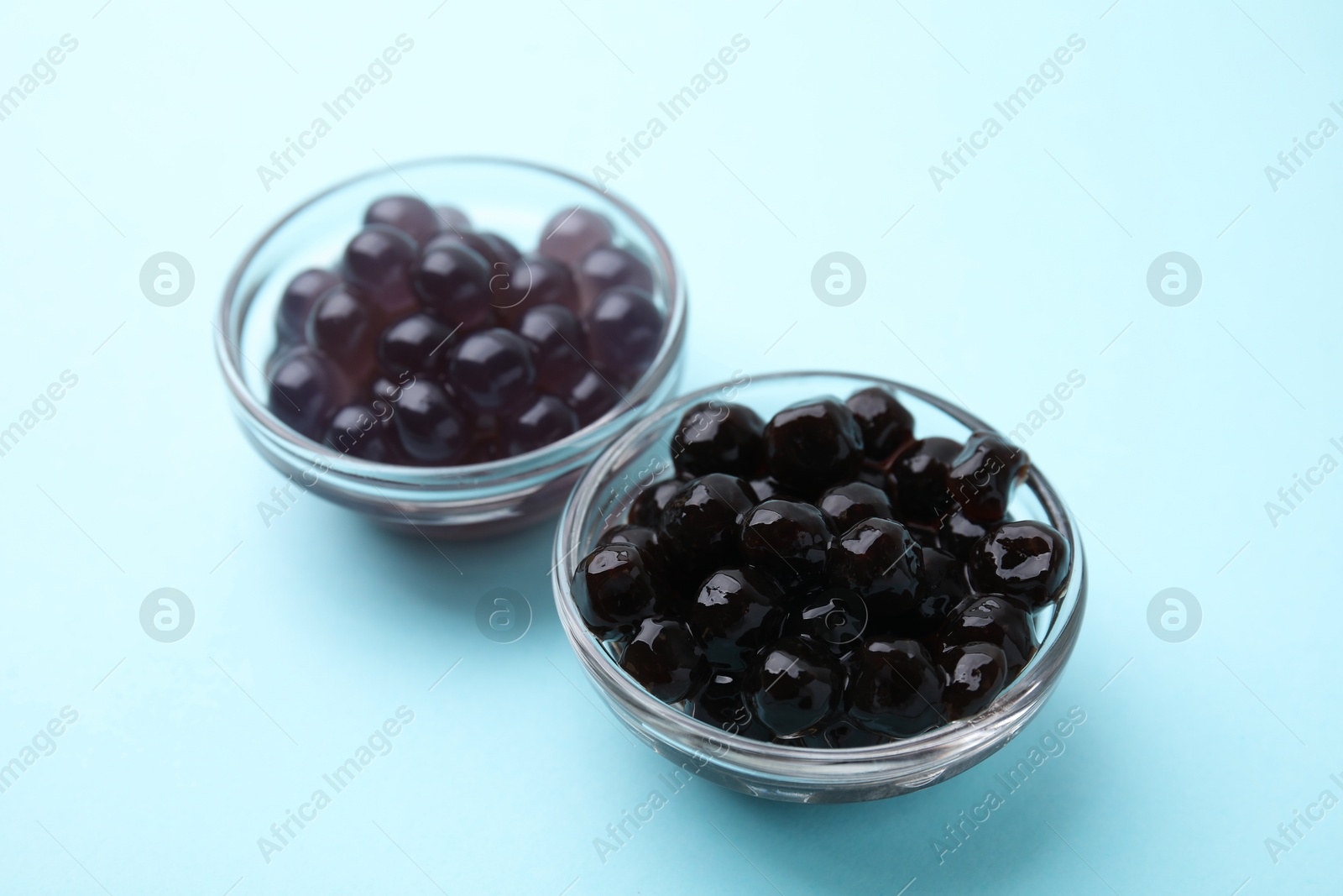 Photo of Dark tapioca pearls in bowls on light blue background, closeup