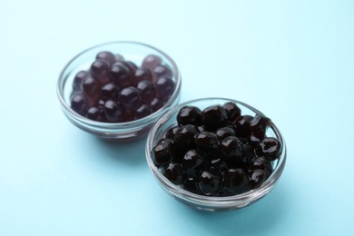 Photo of Dark tapioca pearls in bowls on light blue background, closeup