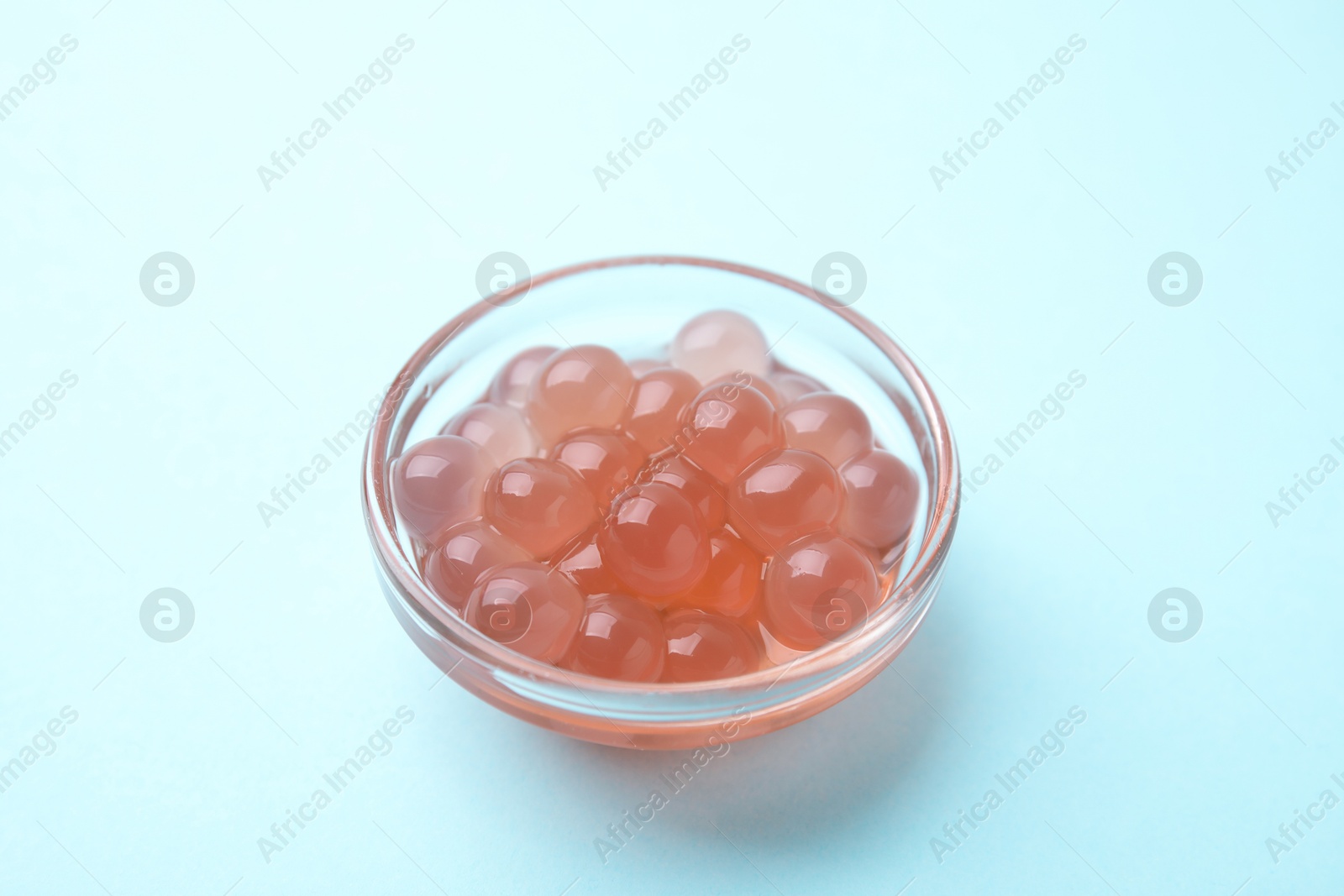 Photo of Bright tapioca pearls in bowl on light blue background, closeup