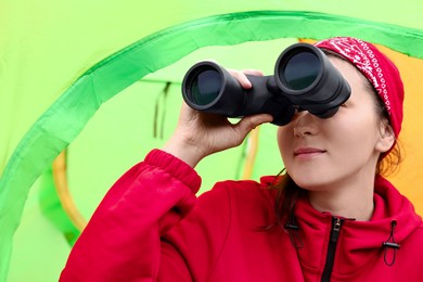 Young woman looking through binoculars near tent outdoors, low angle view