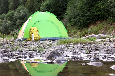 Photo of Camping tent, backpack and thermo bottle on stones near river in mountains