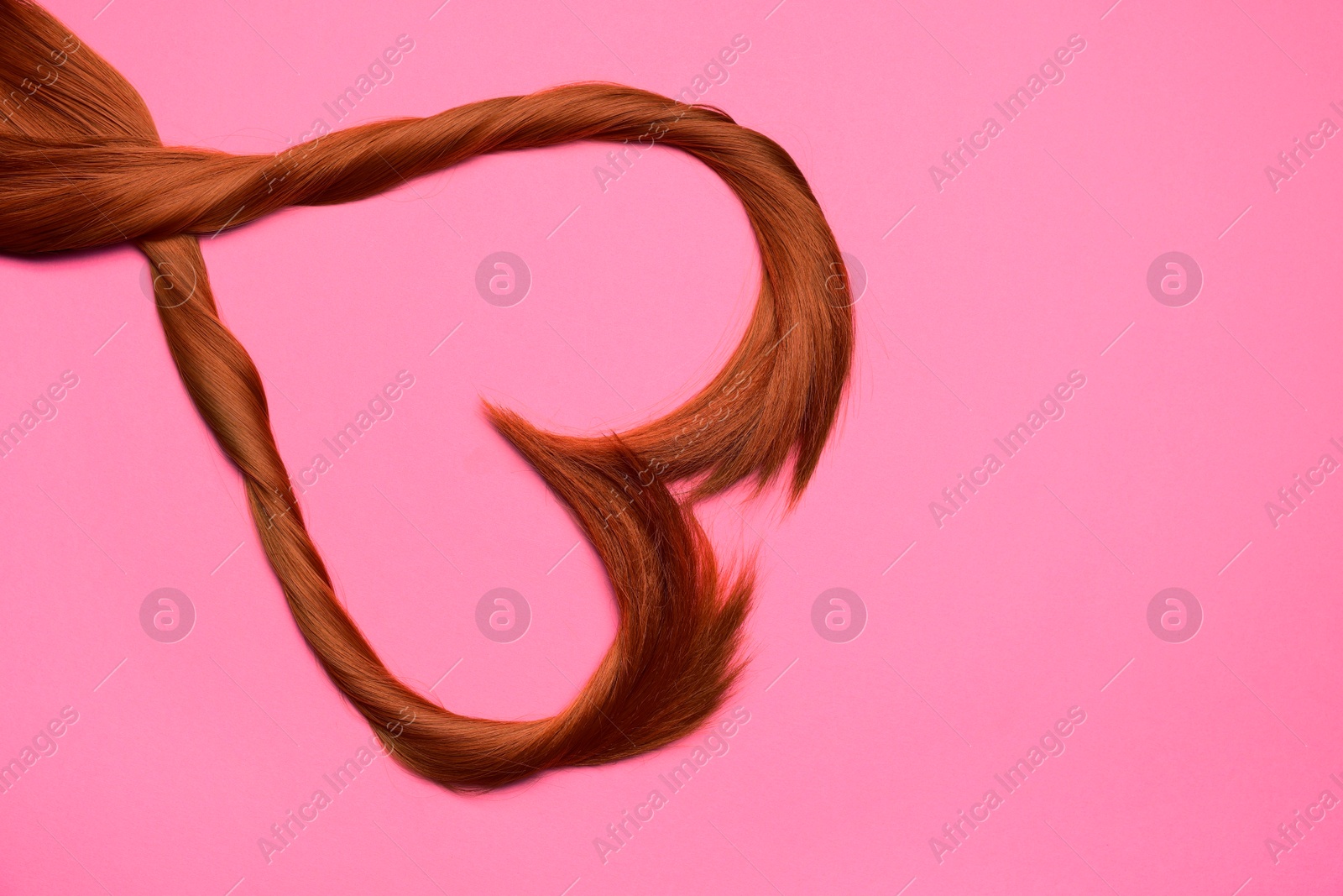 Photo of Red hair strands in shape of heart on pink background, top view. Space for text