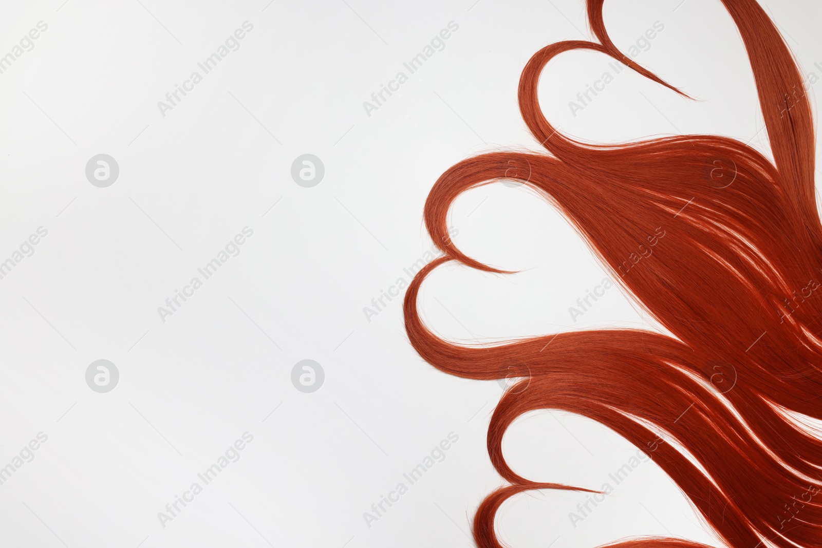 Photo of Red hair strands in shape of hearts on white background, top view. Space for text