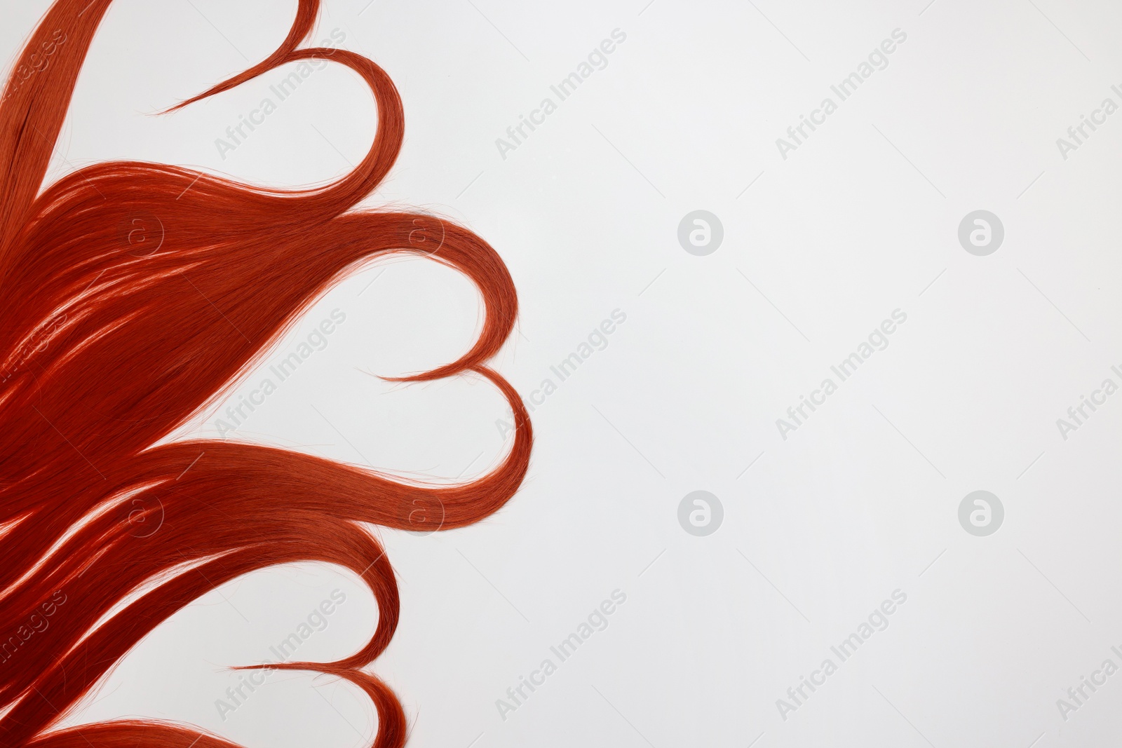 Photo of Red hair strands in shape of hearts on white background, top view. Space for text