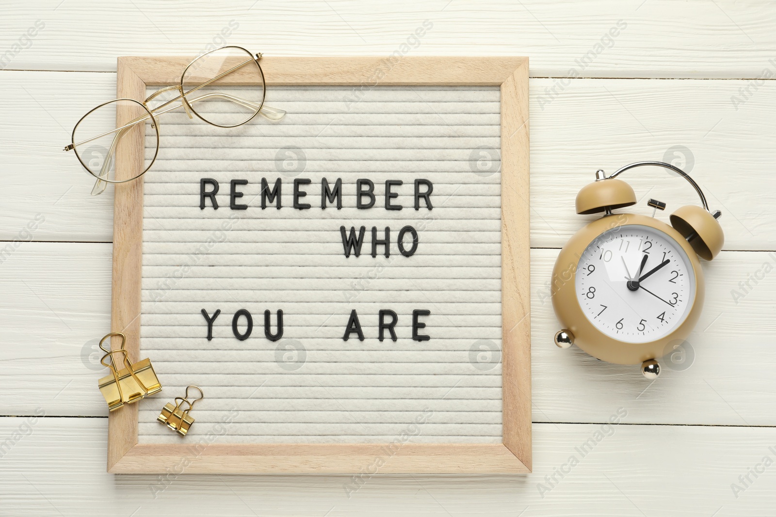 Photo of Letter board with phrase Remember Who You Are, alarm clock, clips and glasses on white wooden table, flat lay