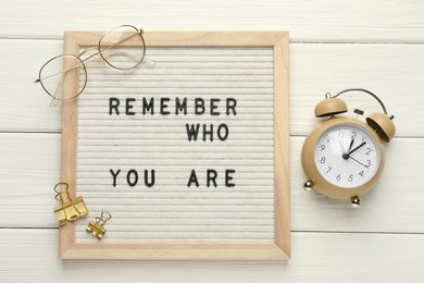 Photo of Letter board with phrase Remember Who You Are, alarm clock, clips and glasses on white wooden table, flat lay