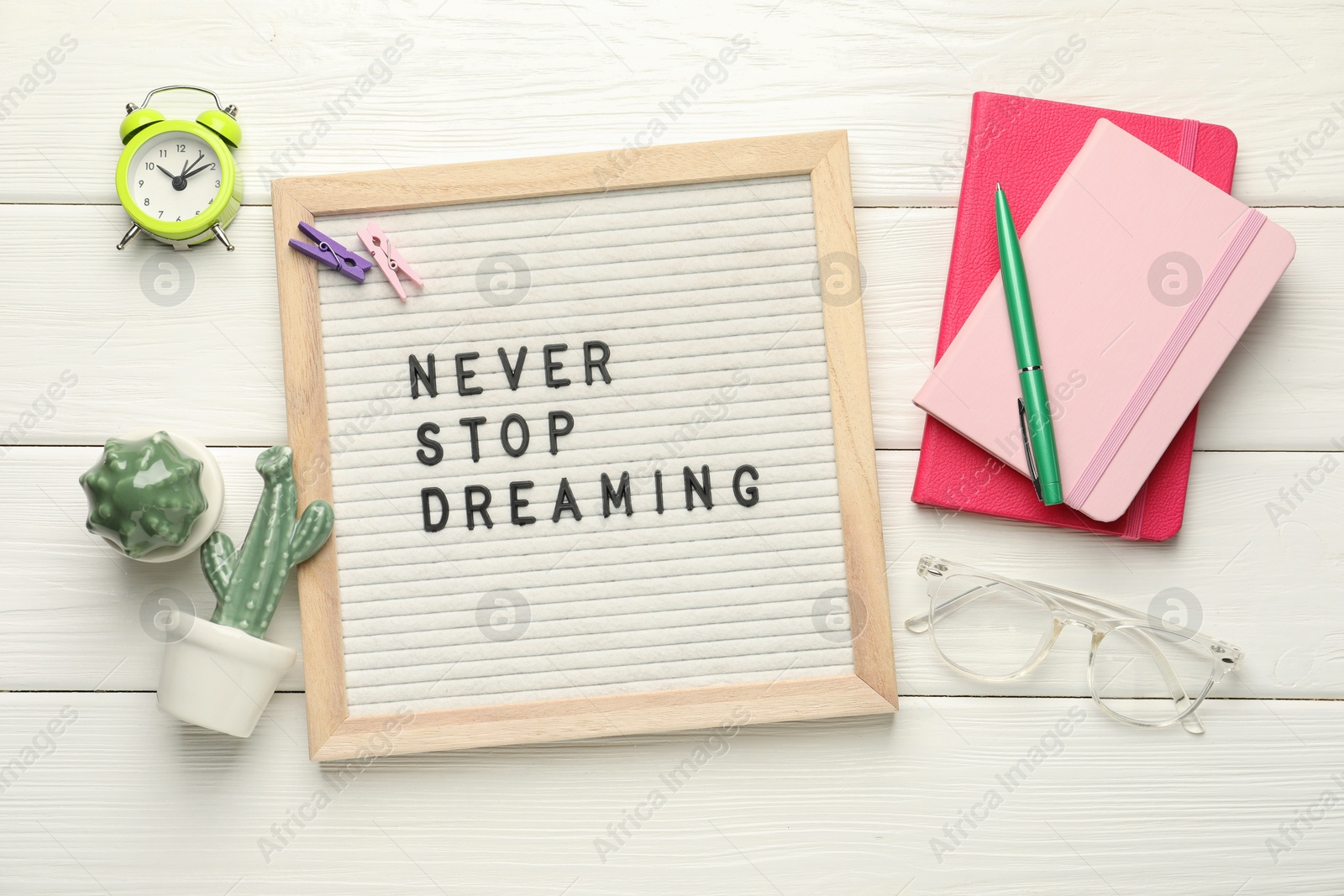 Photo of Letter board with phrase Never Stop Dreaming, glasses, alarm clock and stationery on white wooden table, flat lay