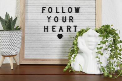 Photo of Letter board with phrase Follow Your Heart and plants on wooden table