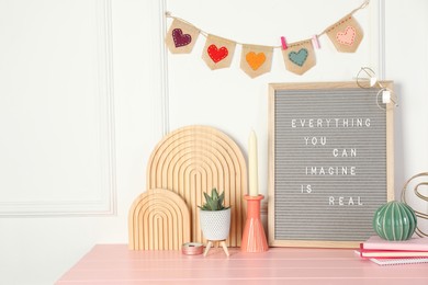 Photo of Letter board with phrase Everything You Can Imagine Is Real and decor elements on pink wooden table. Space for text